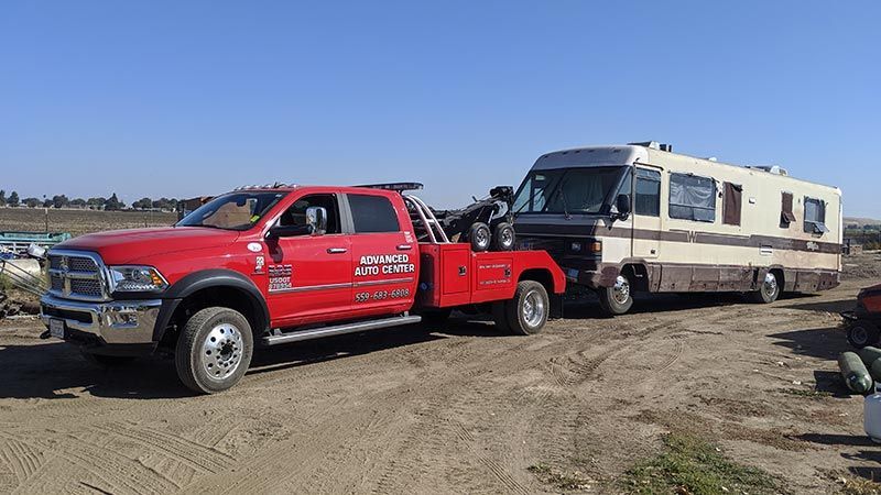 A red tow truck is towing a rv in a dirt field.