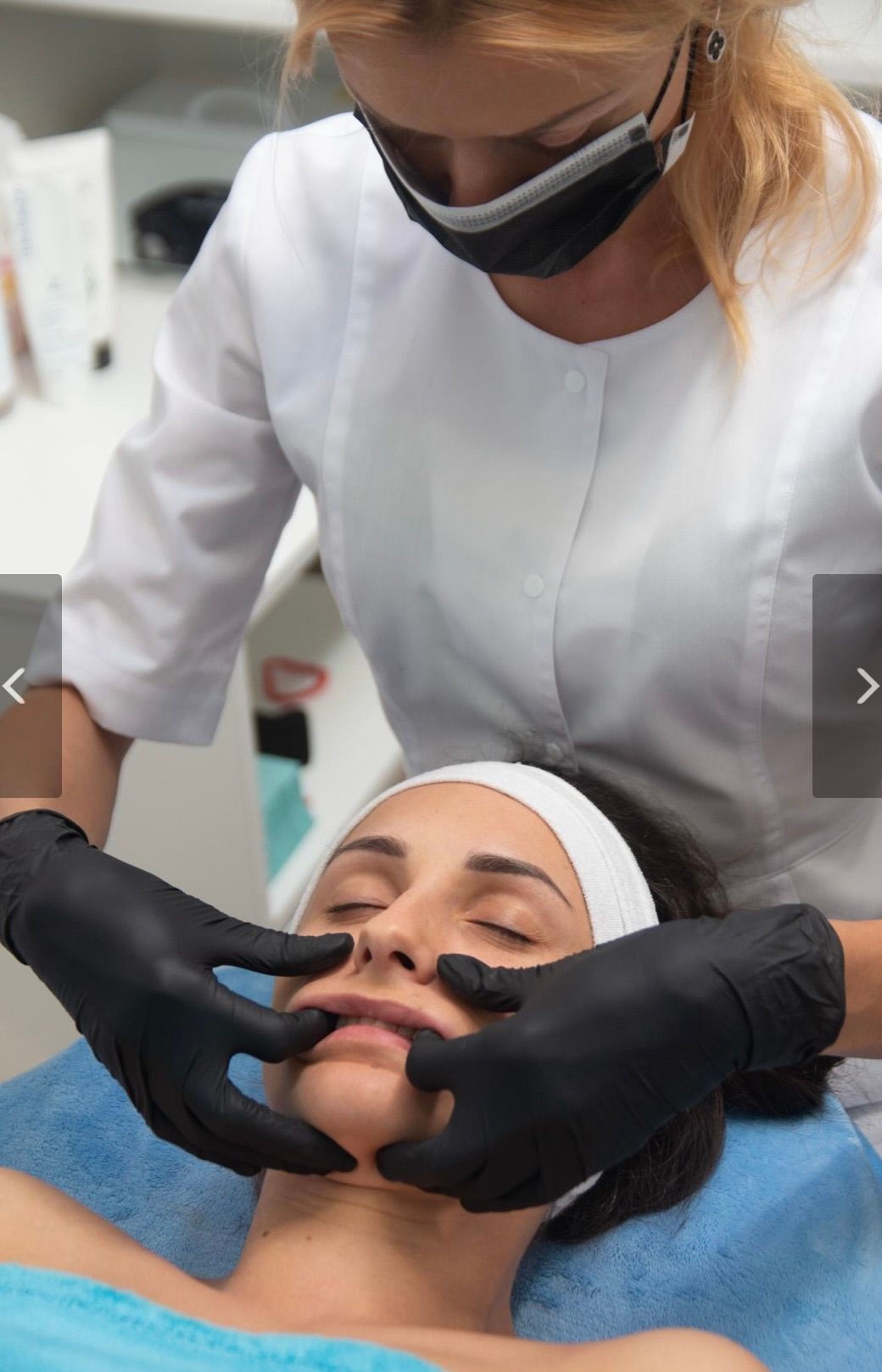 A practitioner in a white coat and black gloves performs an intraoral buccal massage on a client's face.