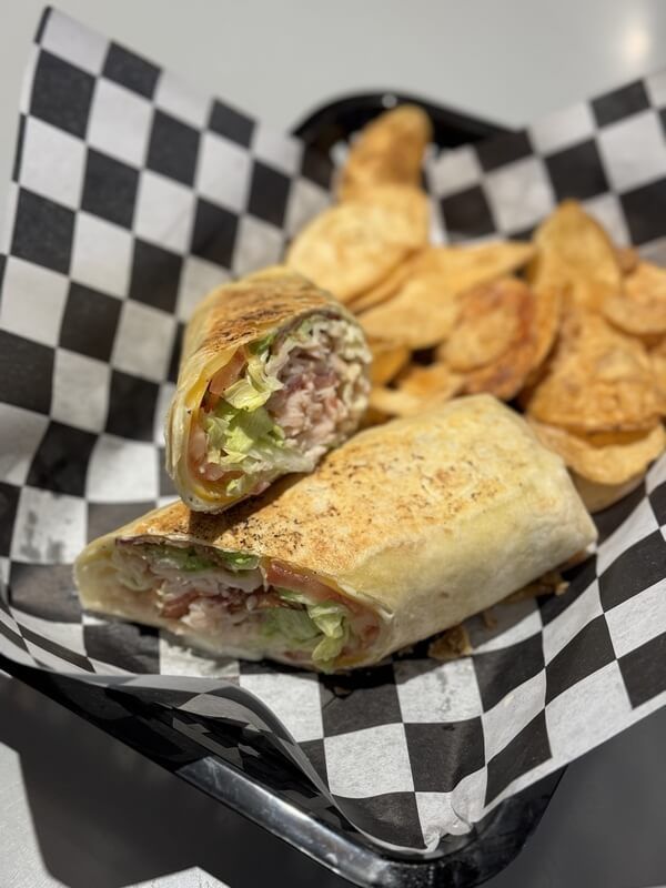 A sandwich and chips in a basket on checkered paper.