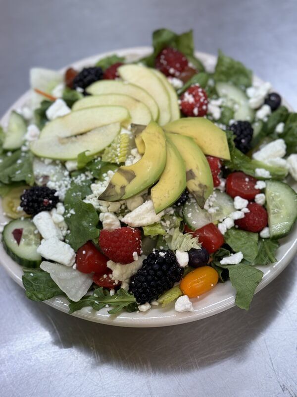 A salad with avocado , apples , raspberries , cucumbers and feta cheese on a plate.