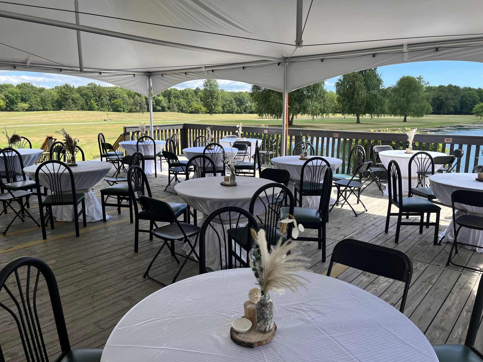 Tables and chairs are set up on a deck under a tent.