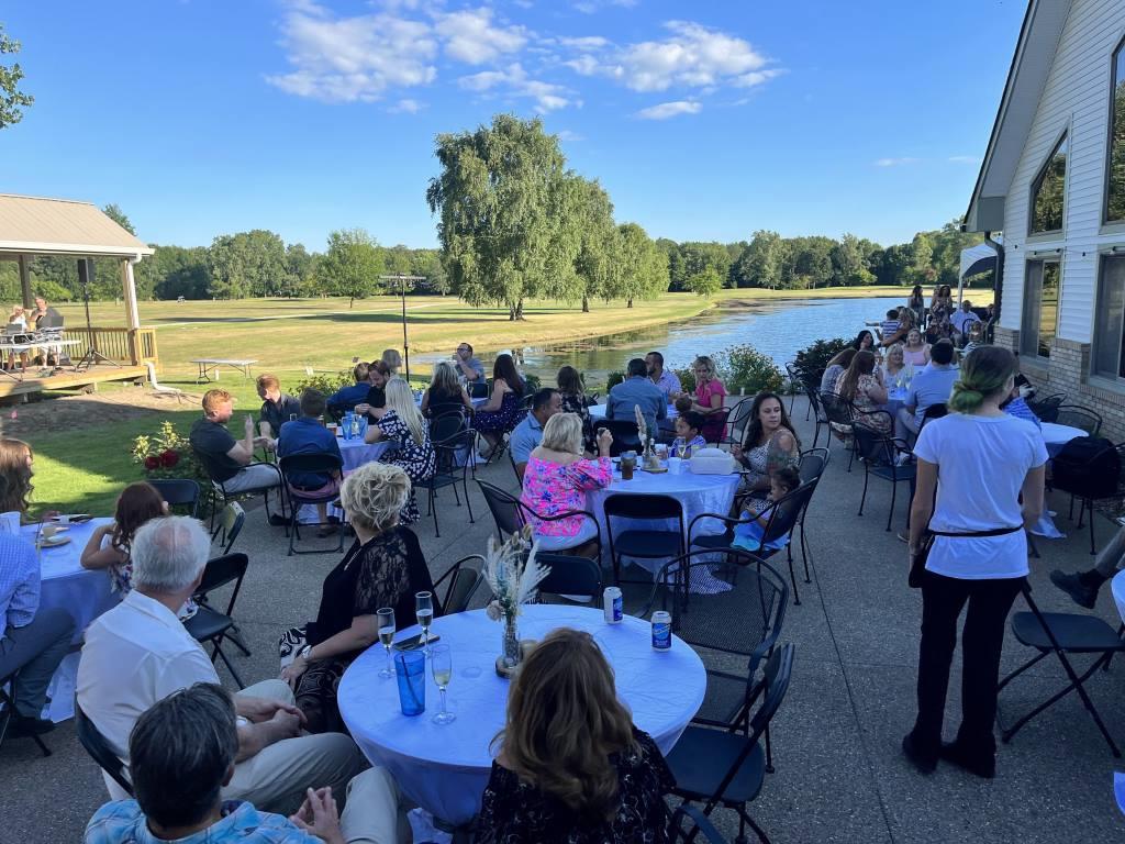 A group of people are sitting at tables in front of a lake