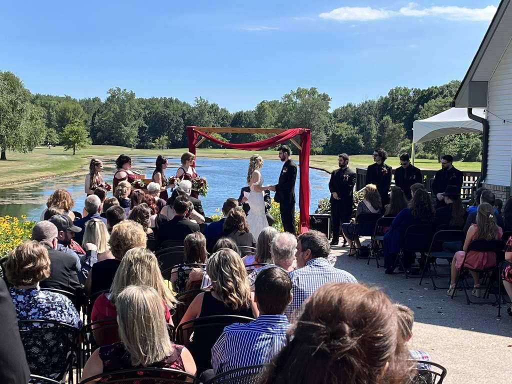 A large group of people are watching a wedding ceremony in front of a lake.