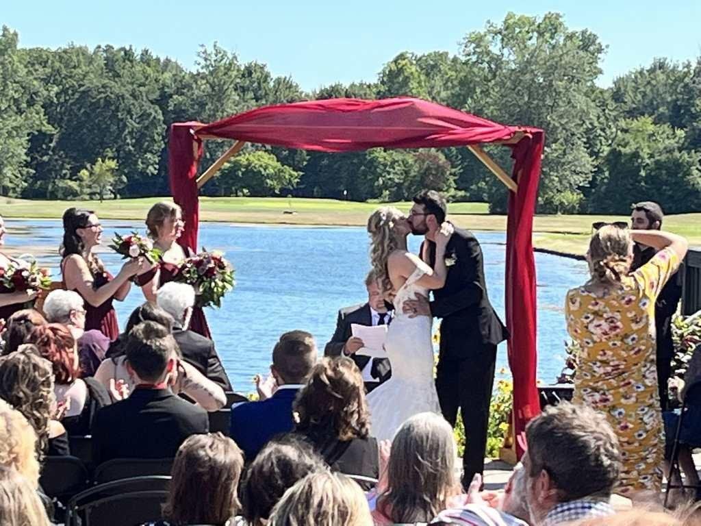 A bride and groom kissing at their wedding ceremony in front of a crowd of people.