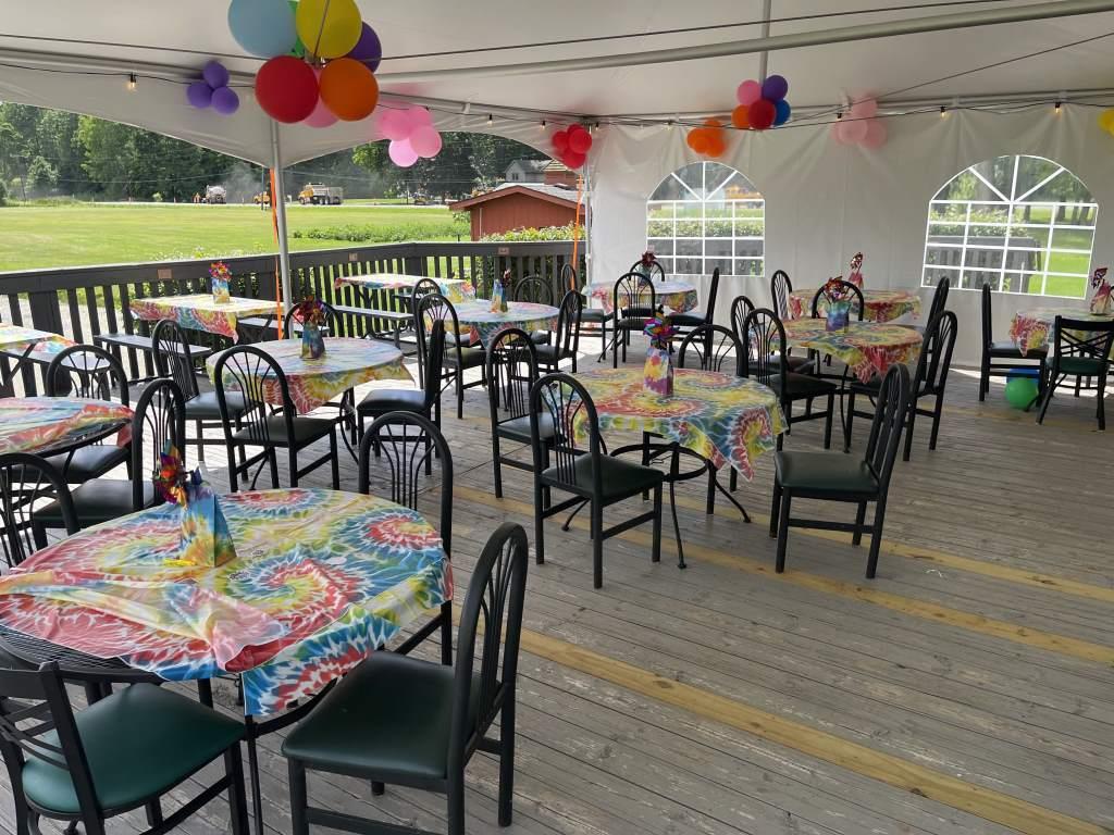 Tables and chairs under a tent with balloons hanging from the ceiling