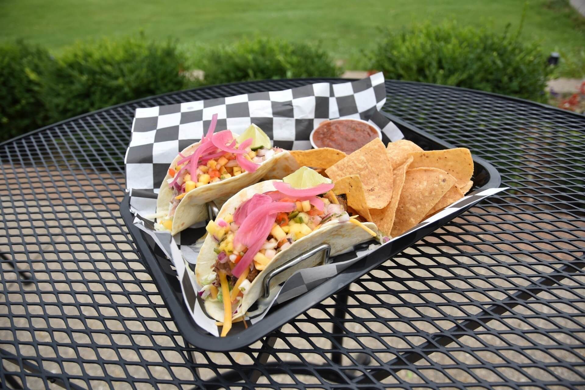 Two tacos and chips are on a tray on a table.
