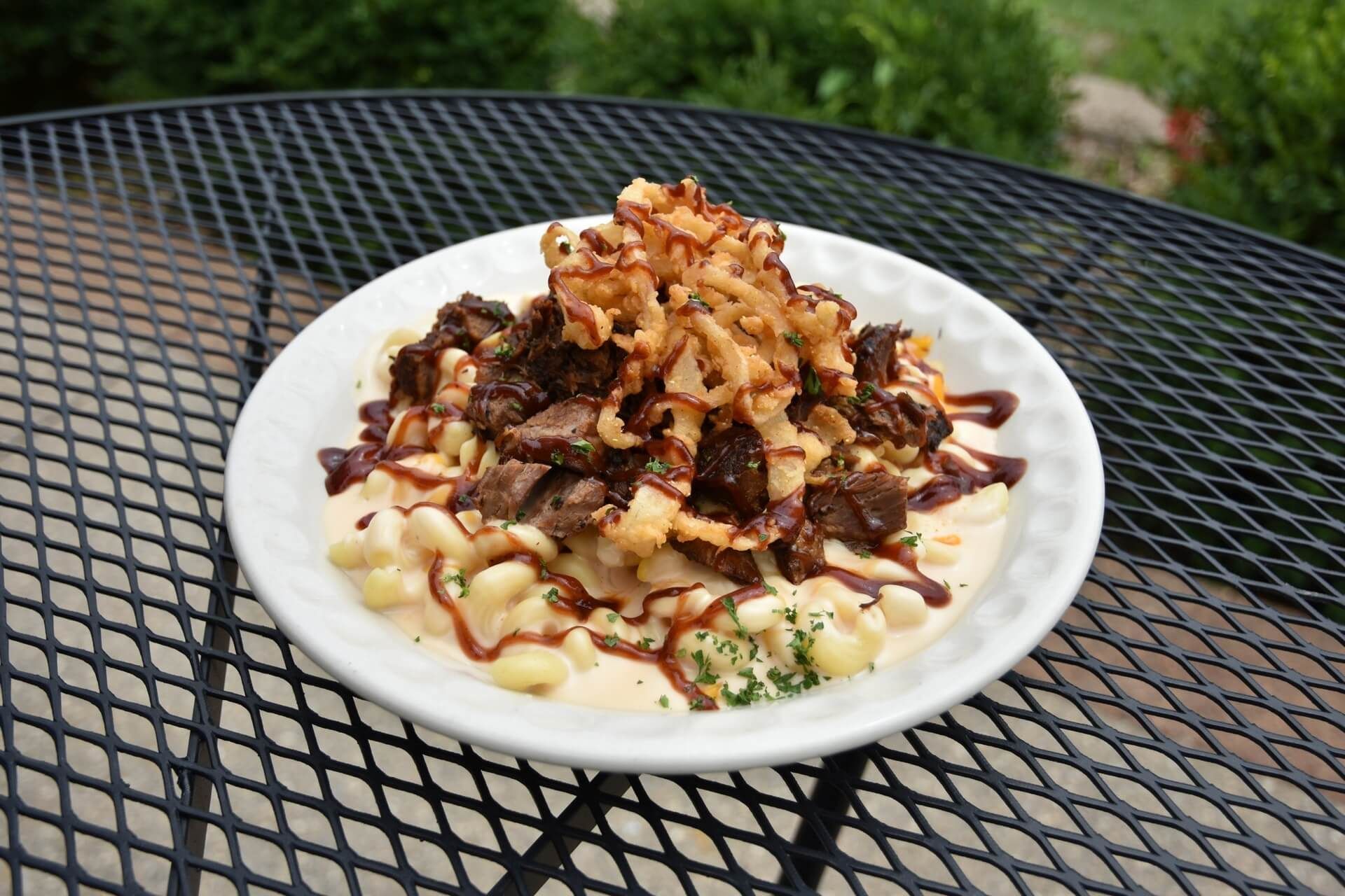 A white plate topped with macaroni and cheese and meat on a metal table.