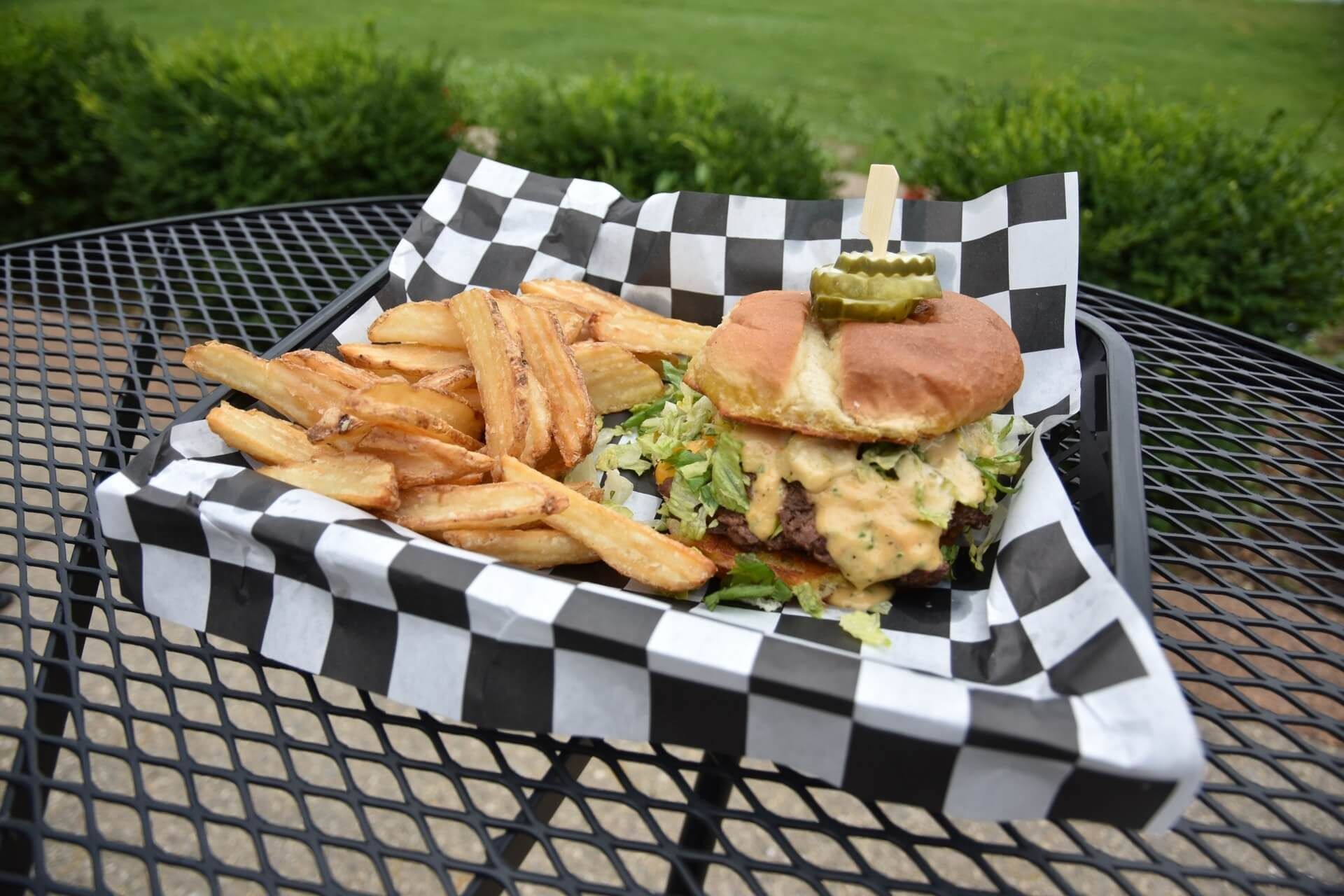 A hamburger and french fries on a checkered paper on a table.
