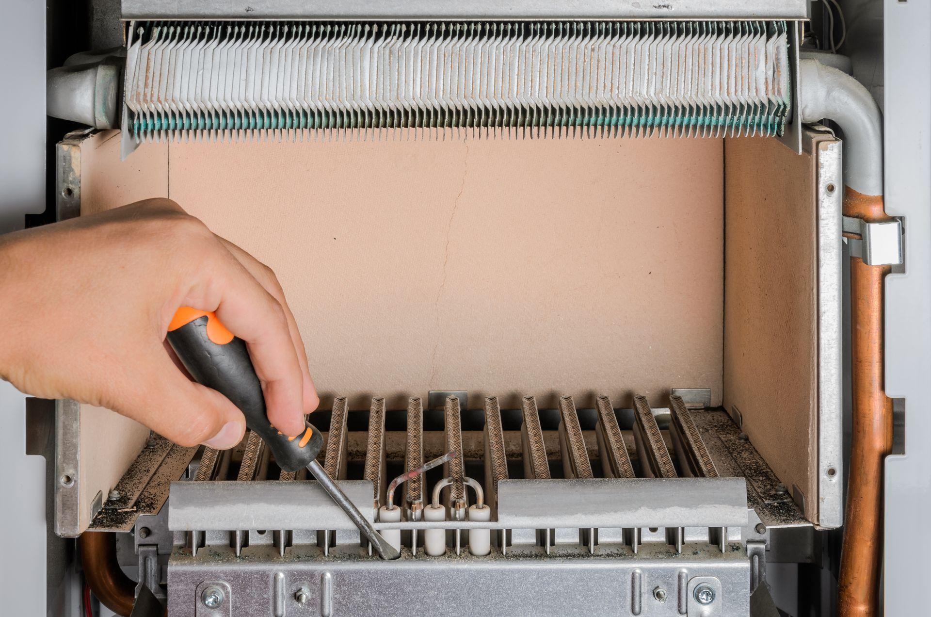 Hand using a screwdriver to inspect a furnace with exposed components.