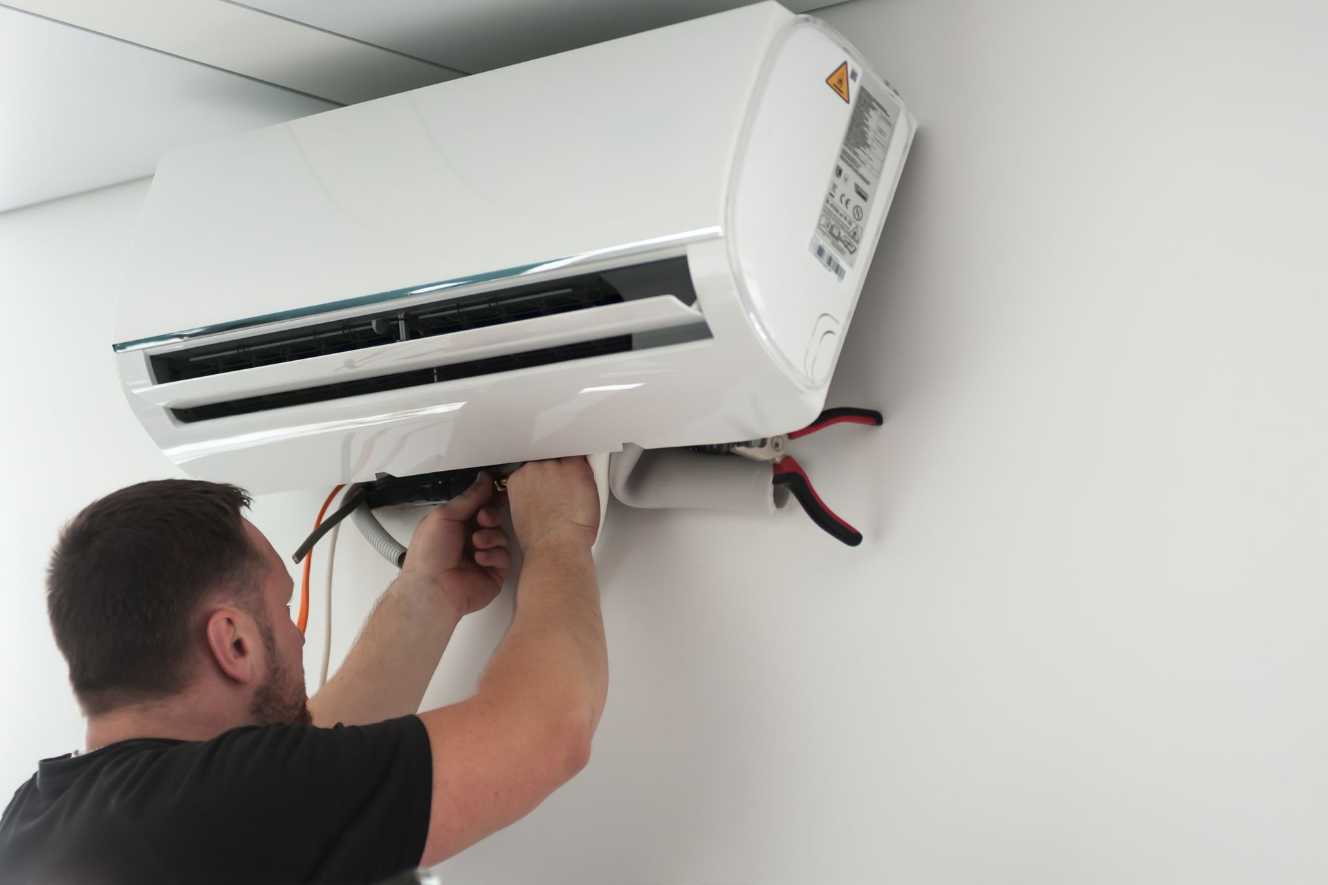 Person working on an air conditioner mounted on a white wall.