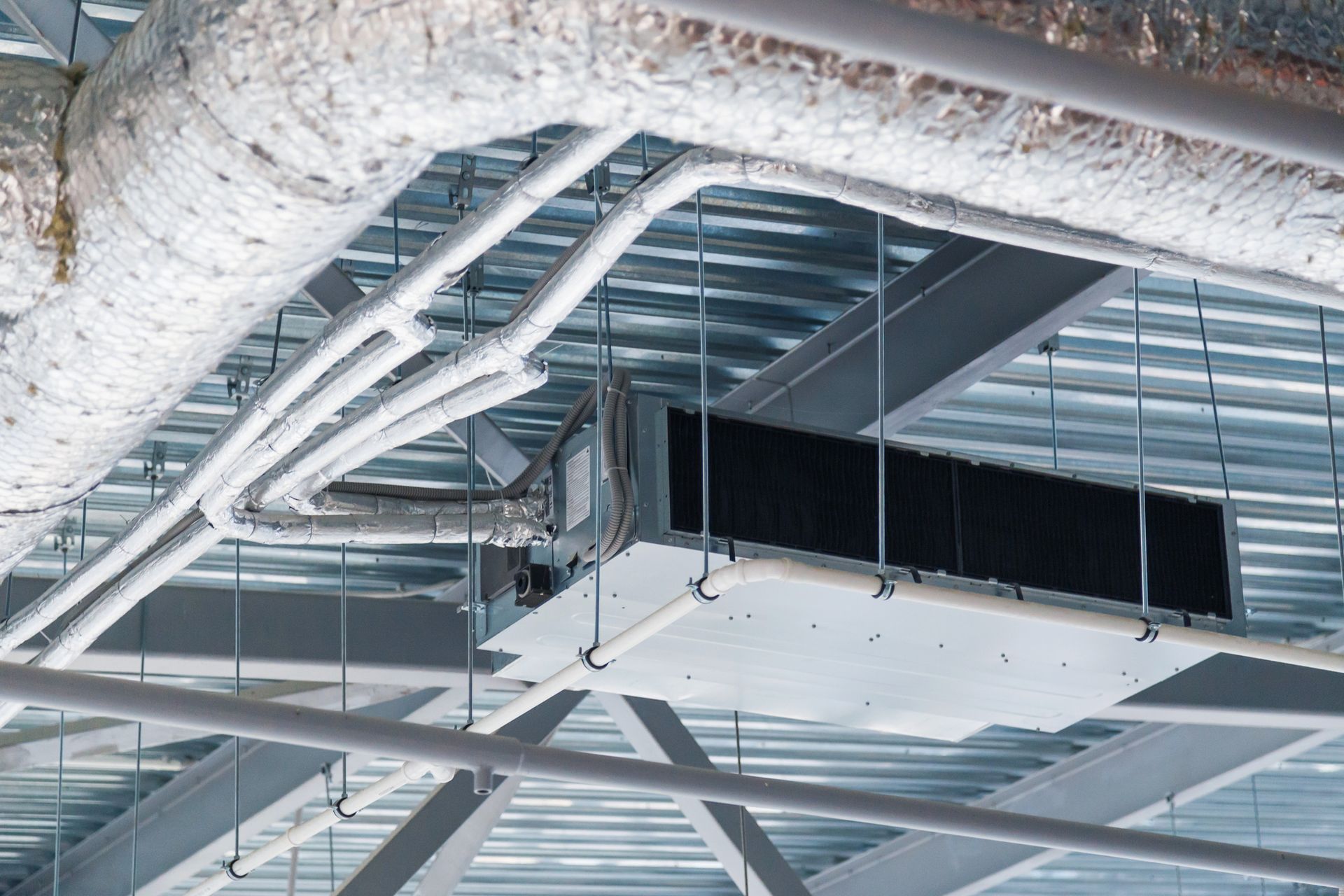 HVAC unit suspended from a steel beam ceiling, with pipes and ductwork.