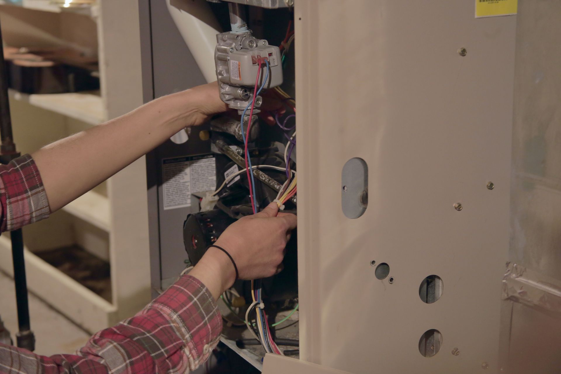 Person working on the interior of a furnace, with hands on wiring.