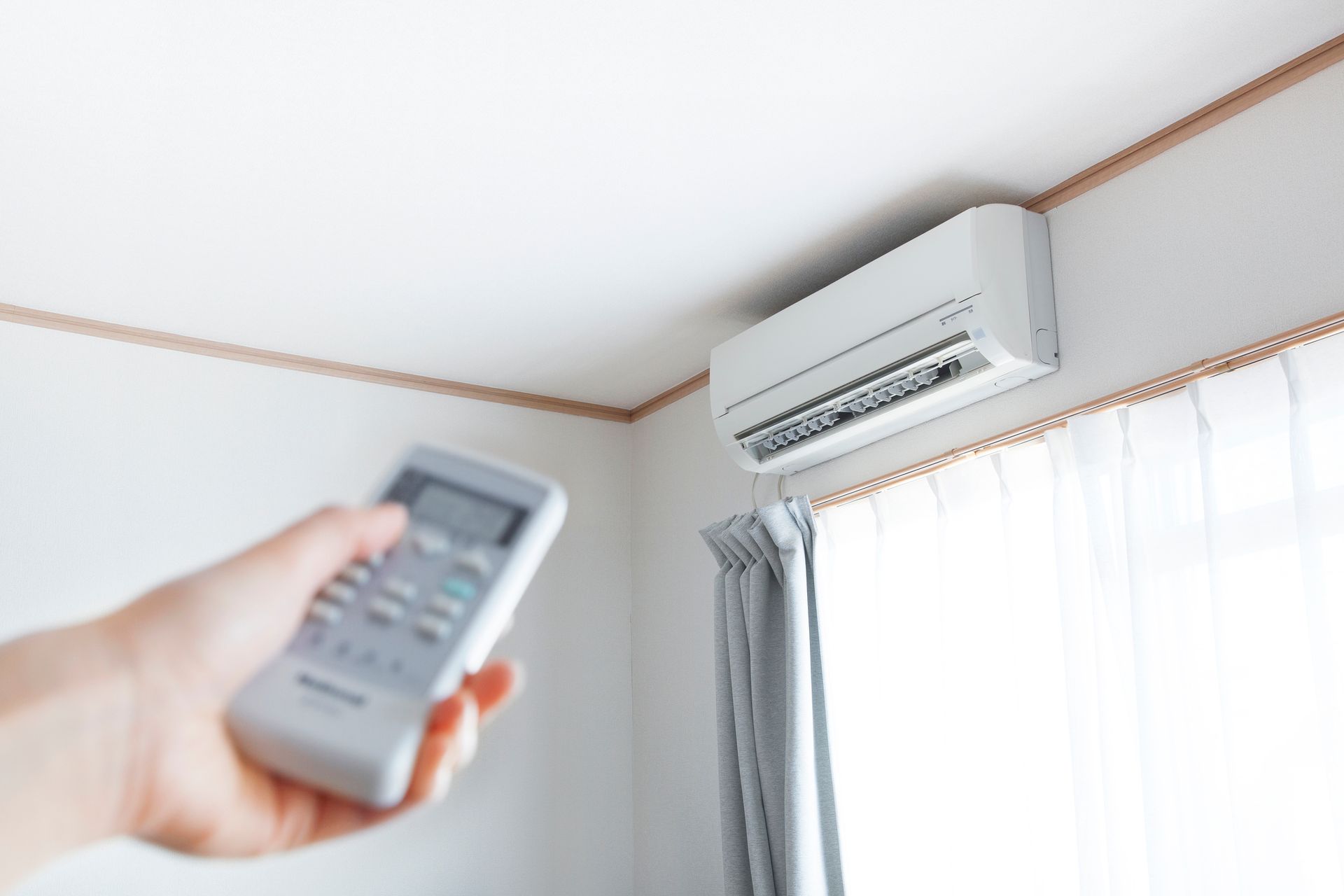 Person using remote to operate a white wall-mounted air conditioner in a room.