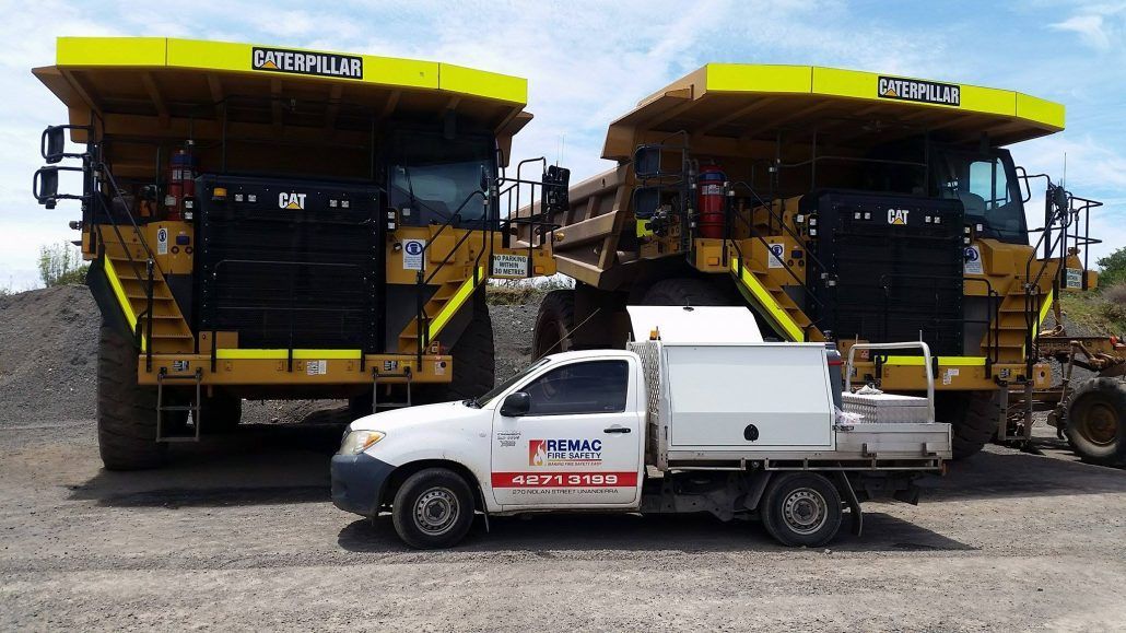 A white truck is parked next to two large yellow dump trucks.
