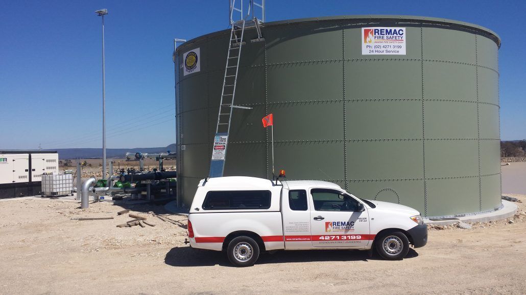 A white truck is parked in front of a large green tank.