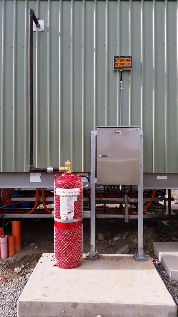 A red fire extinguisher is sitting on a concrete platform in front of a green building.