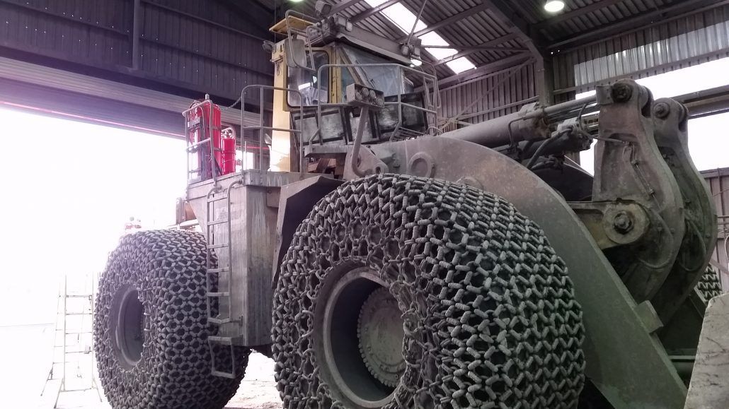 A large tractor with chains on the tires is parked in a warehouse.