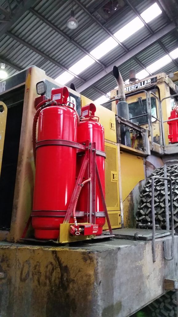 Two red fire extinguishers are attached to the side of a yellow truck.