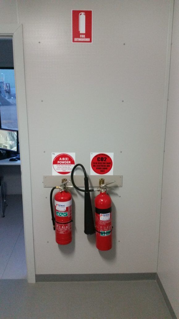 Two fire extinguishers are hanging on a wall in a room.