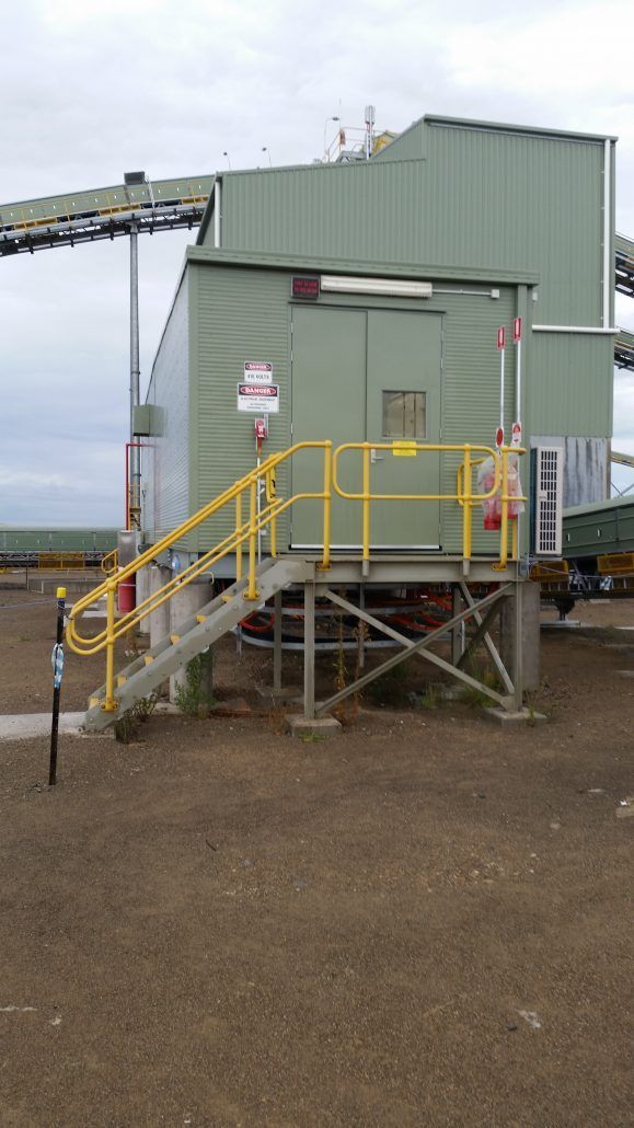 A green building with a yellow railing and stairs leading up to it.