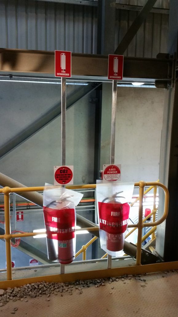 There are two fire extinguishers hanging from the ceiling of a building.