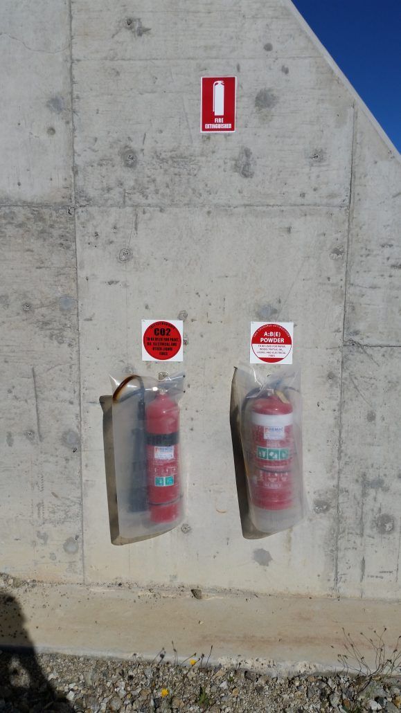 Two fire extinguishers are hanging on a concrete wall.