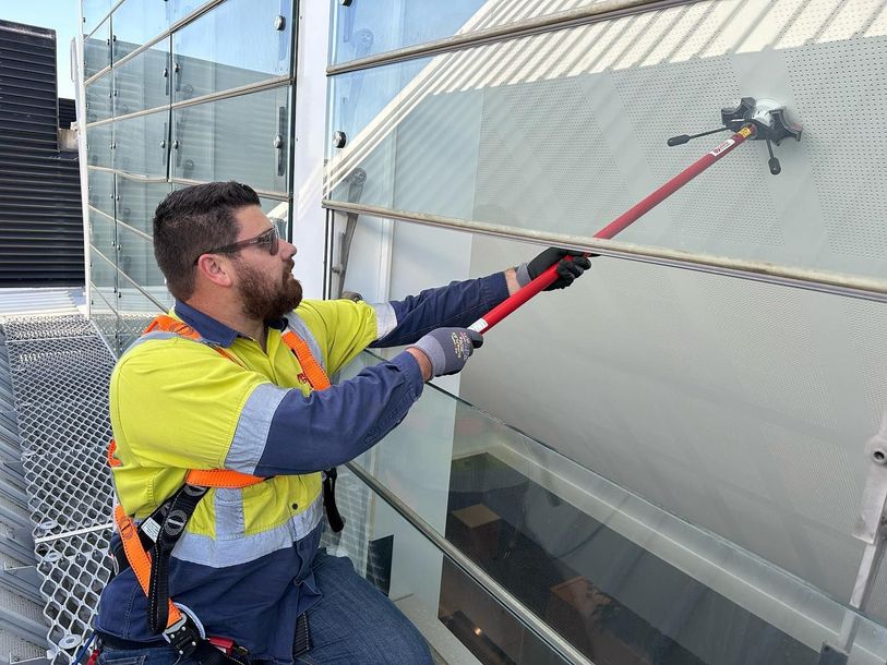 A man is cleaning a building with a long pole.