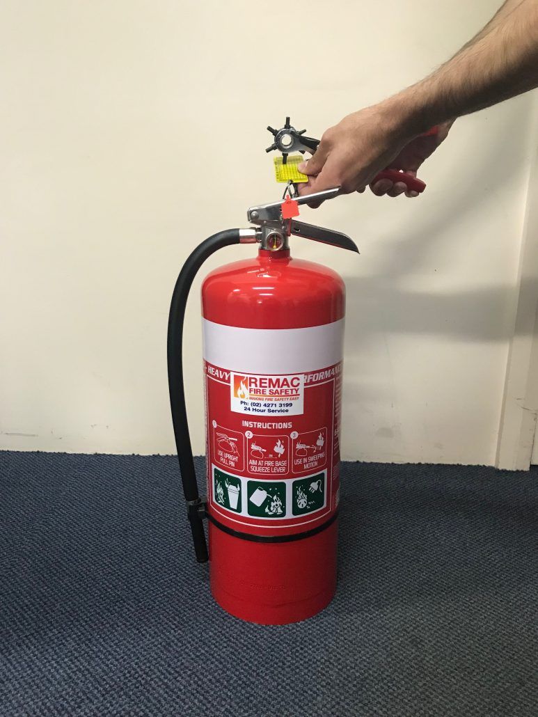 A person is holding a red fire extinguisher on a blue carpet.