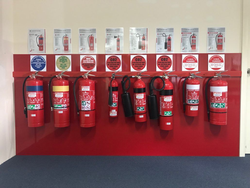 A row of fire extinguishers hanging on a red wall.