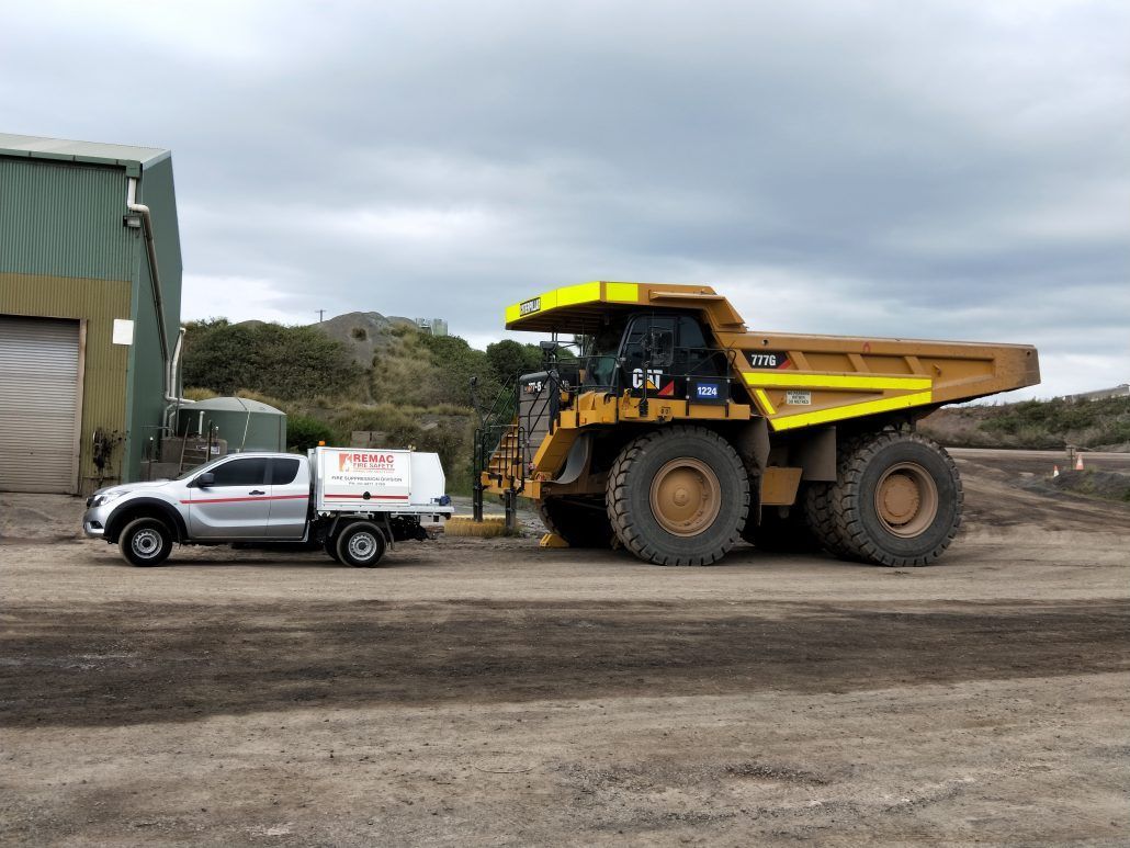 A truck is towing a large dump truck in a dirt field.