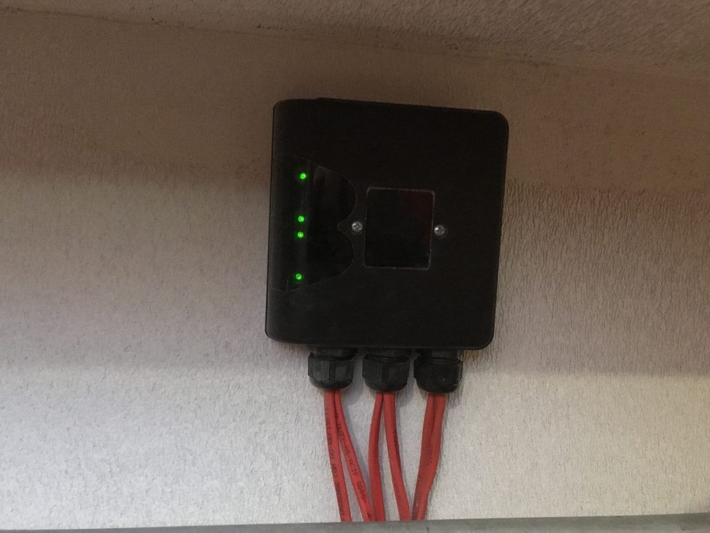A black box with red wires coming out of it is hanging on a wall.