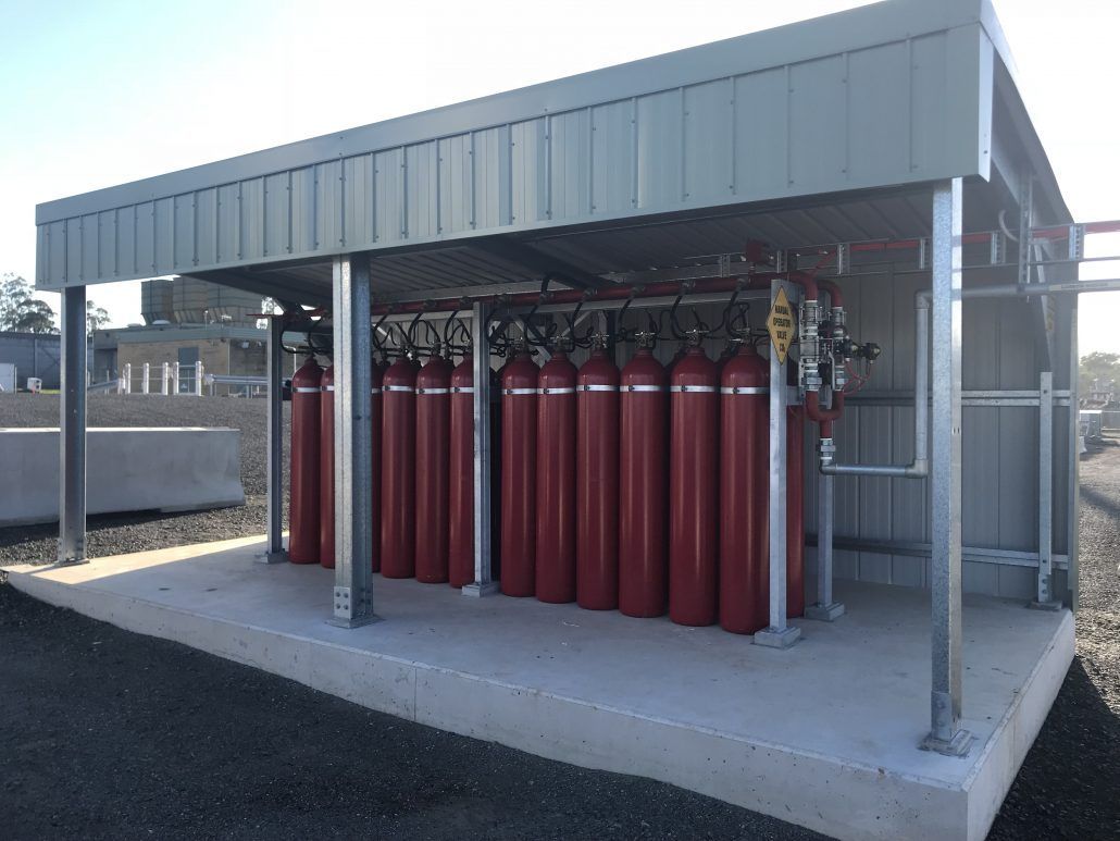 A row of red gas cylinders are lined up in a shed.