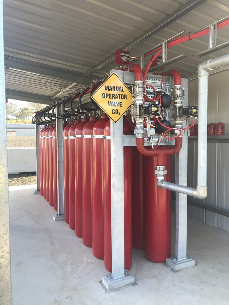 A row of red gas cylinders are lined up under a roof.