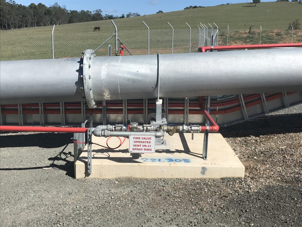 A large pipe is sitting on the ground next to a fence.
