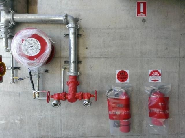 A concrete wall with red pipes and fire extinguishers
