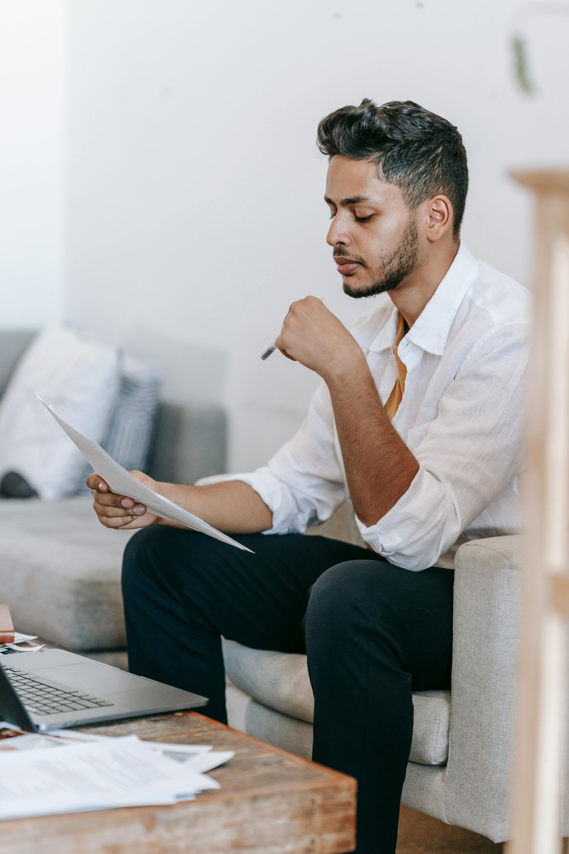 A man is sitting on a couch looking at a piece of paper.