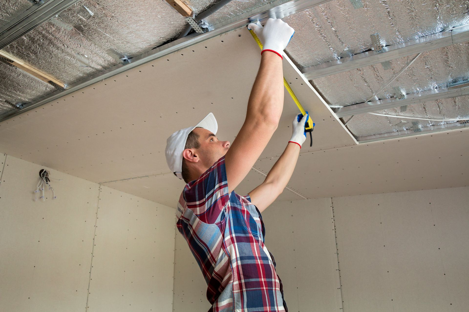 A technician takes a measurement of a drywall-suspended ceiling. A technician takes a measurement of a drywall-suspended ceiling.