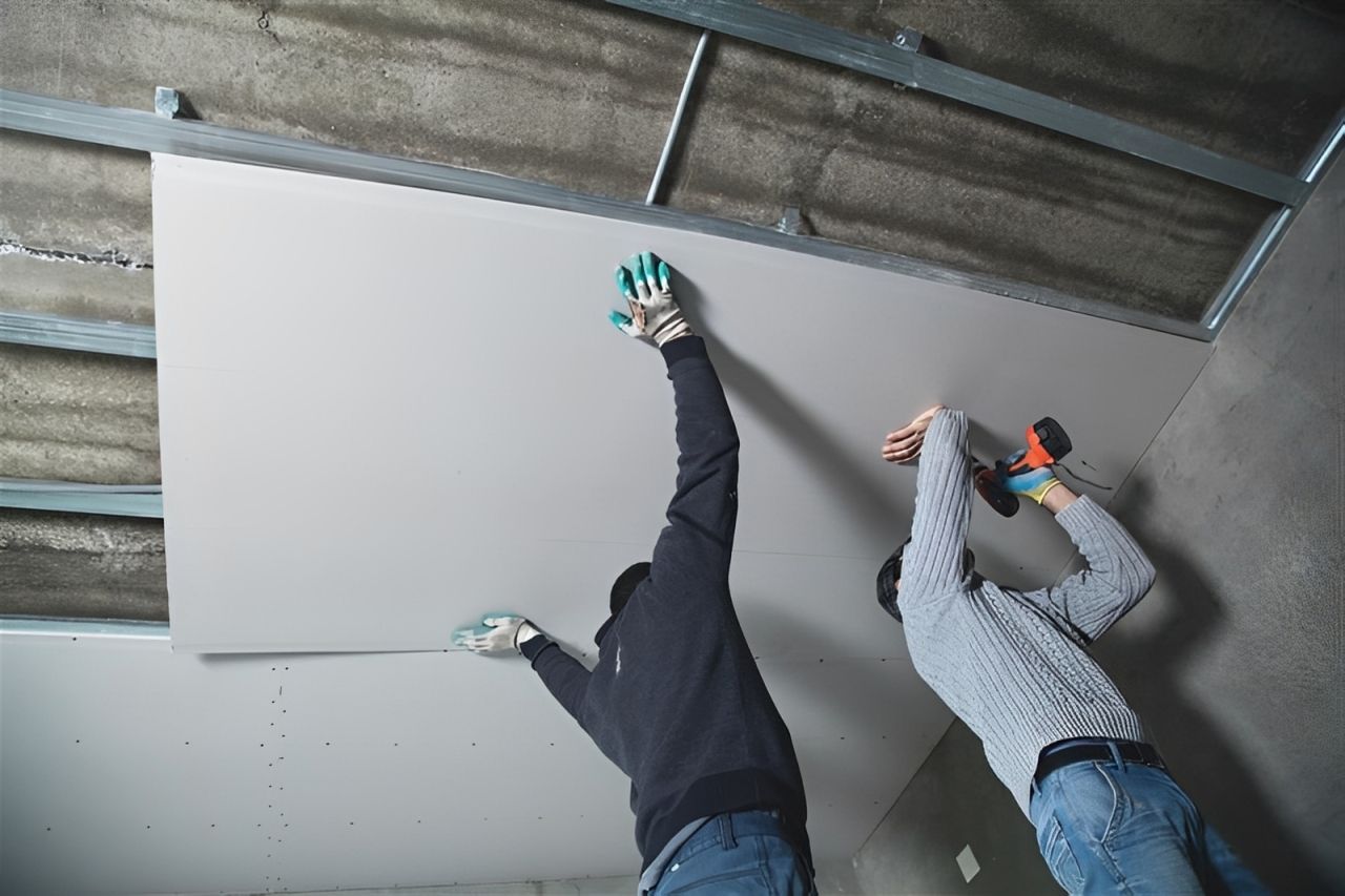 Two contractors fitting a large panel into the frame of a ceiling.