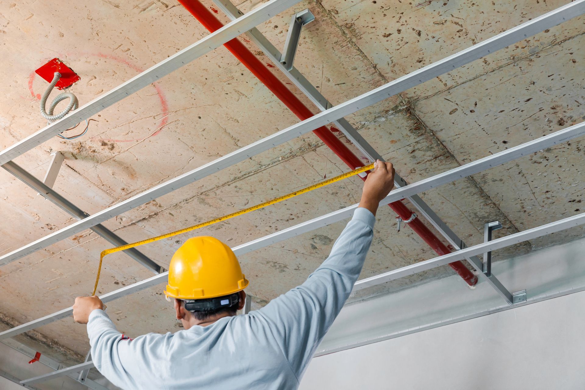 A contractor measuring the distance of a ceiling installation with acoustic panels.