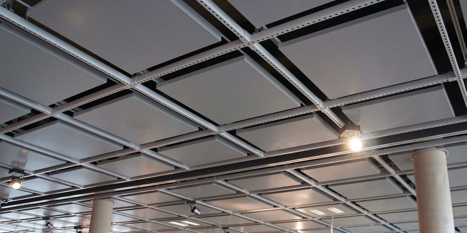 Grid-like ceiling with metal panels. Bright lights are visible. Grid-like ceiling with metal panels. Bright lights are visible.
