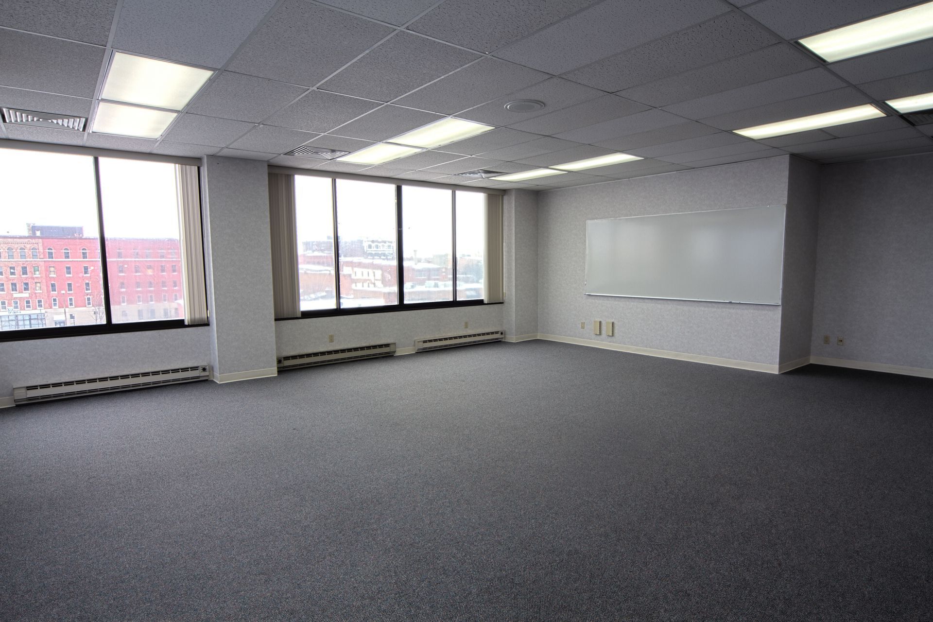 Empty office room with large windows, white board, and dark carpet. Empty office room with large windows, white board, and dark carpet.