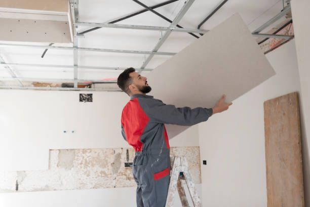 Worker installs drop ceiling panel into metal grid in room under renovation.