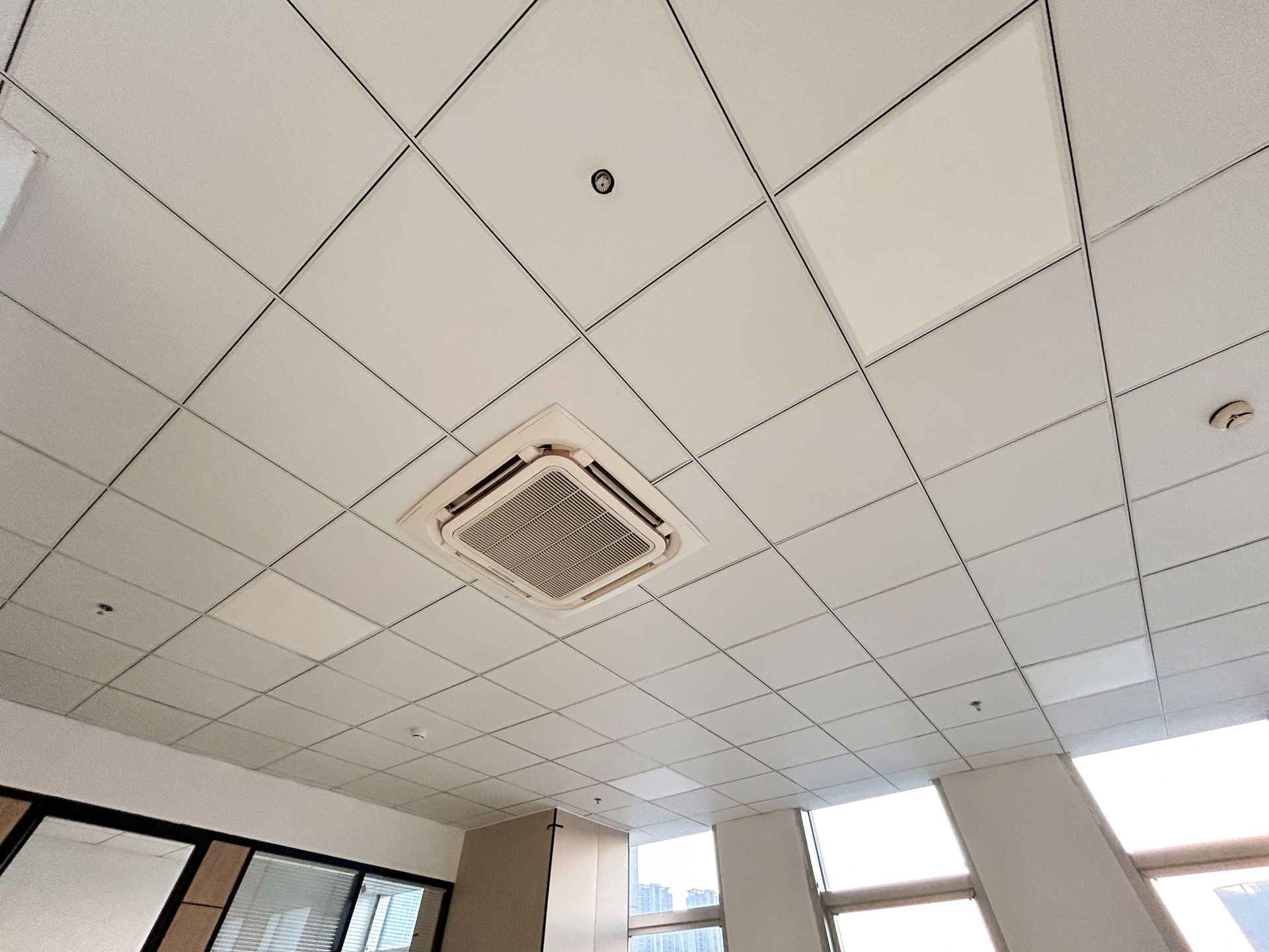 Suspended ceiling with grid panels and a built-in air conditioning unit in a modern space.