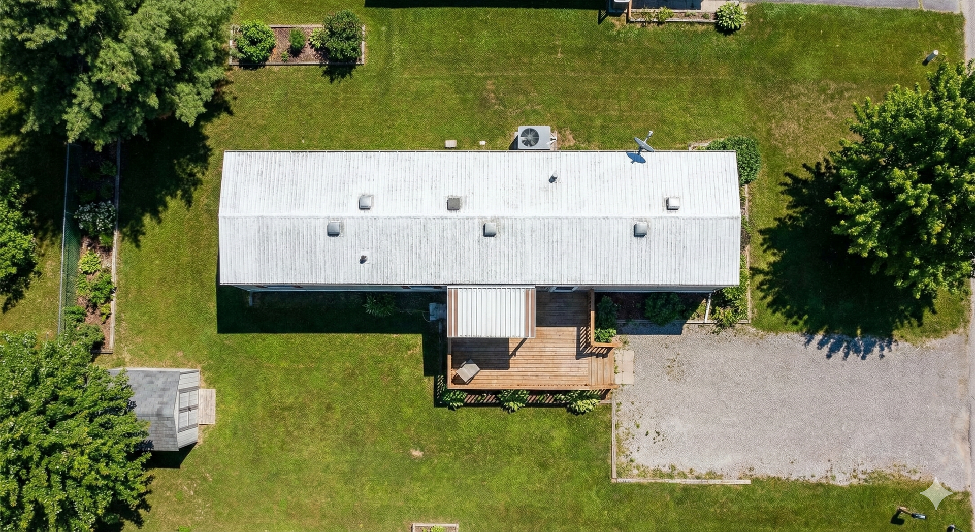 Overhead view of a rectangular, weathered mobile home with a small wooden deck and gravel parking area.