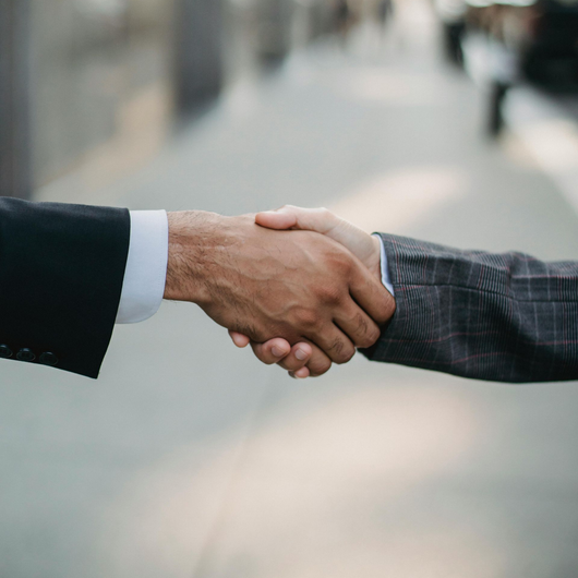 Two men in suits shaking hands outdoors.