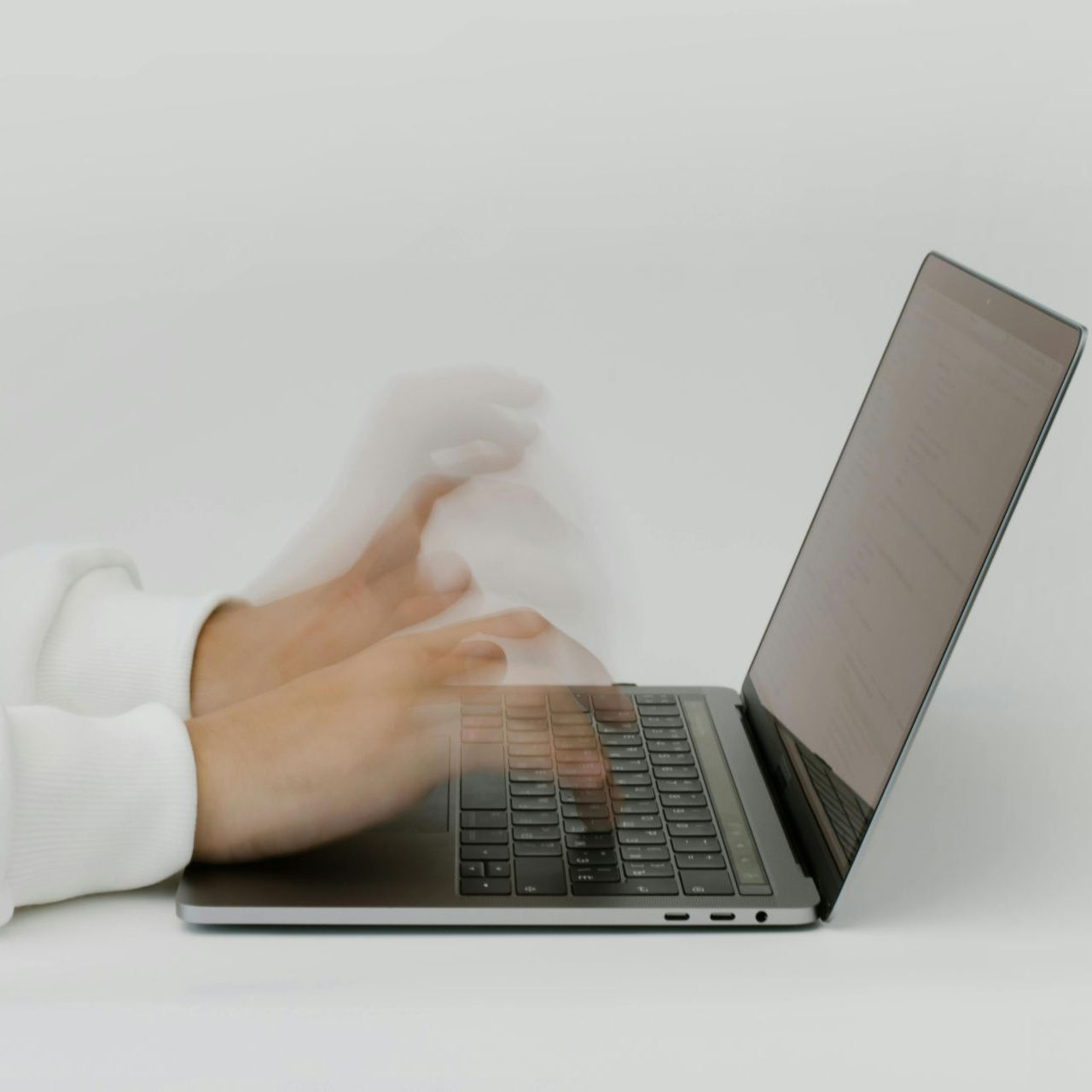 Hands typing rapidly on a laptop keyboard; motion blur suggests speed, white background.