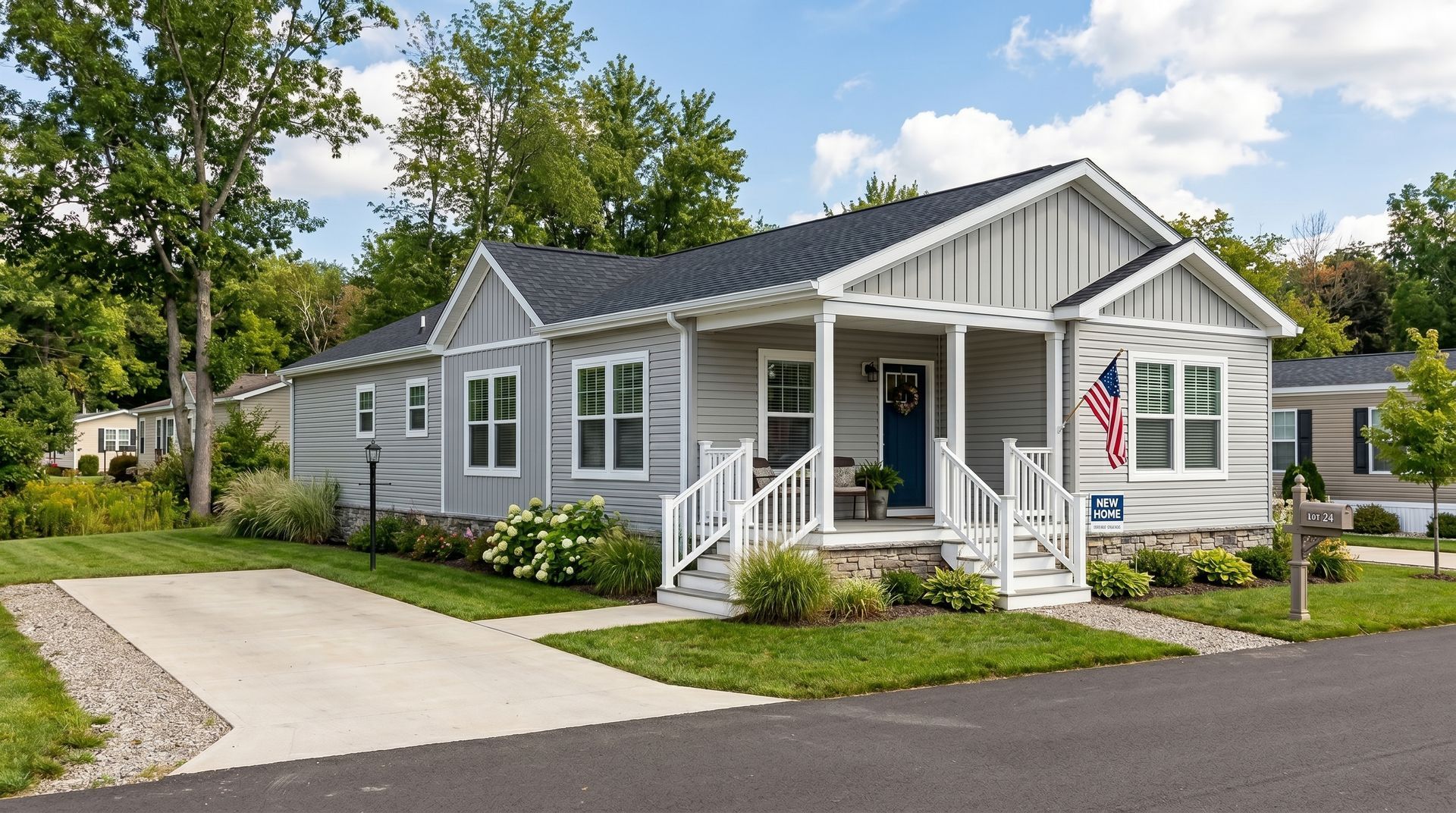 Gray bungalow-style house with white trim, front porch, and a driveway amid trees on a sunny day