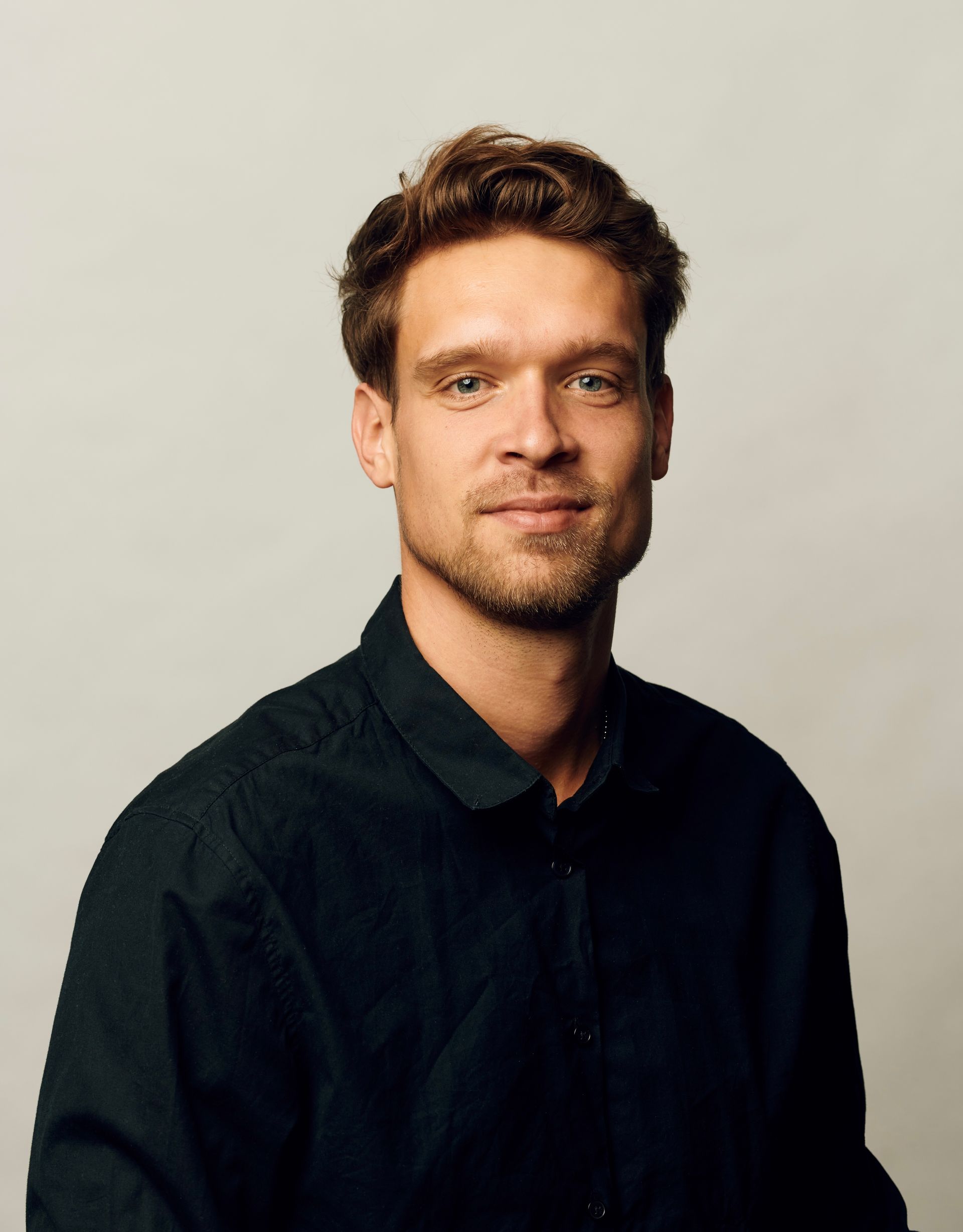 A man with a beard is wearing a black shirt and smiling for the camera.