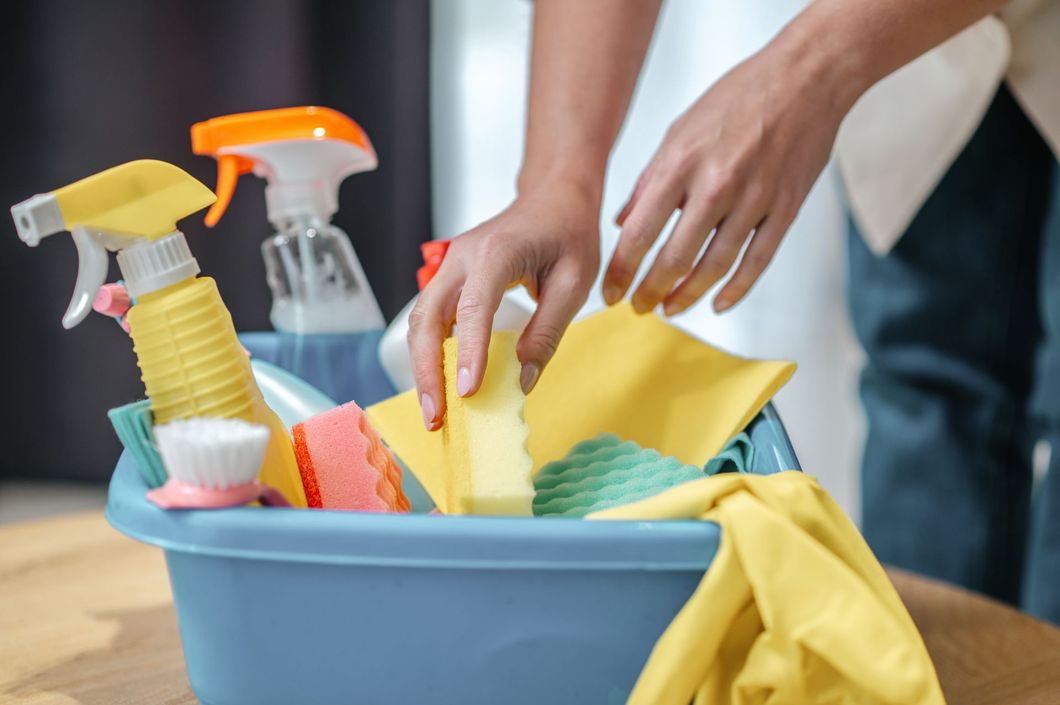 A person is cleaning a blue bucket filled with cleaning supplies.