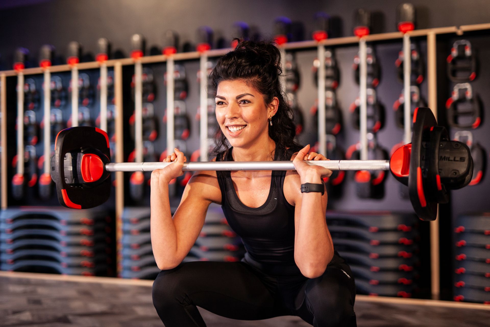 Een vrouw hurkt met een halter boven haar hoofd in een sportschool.